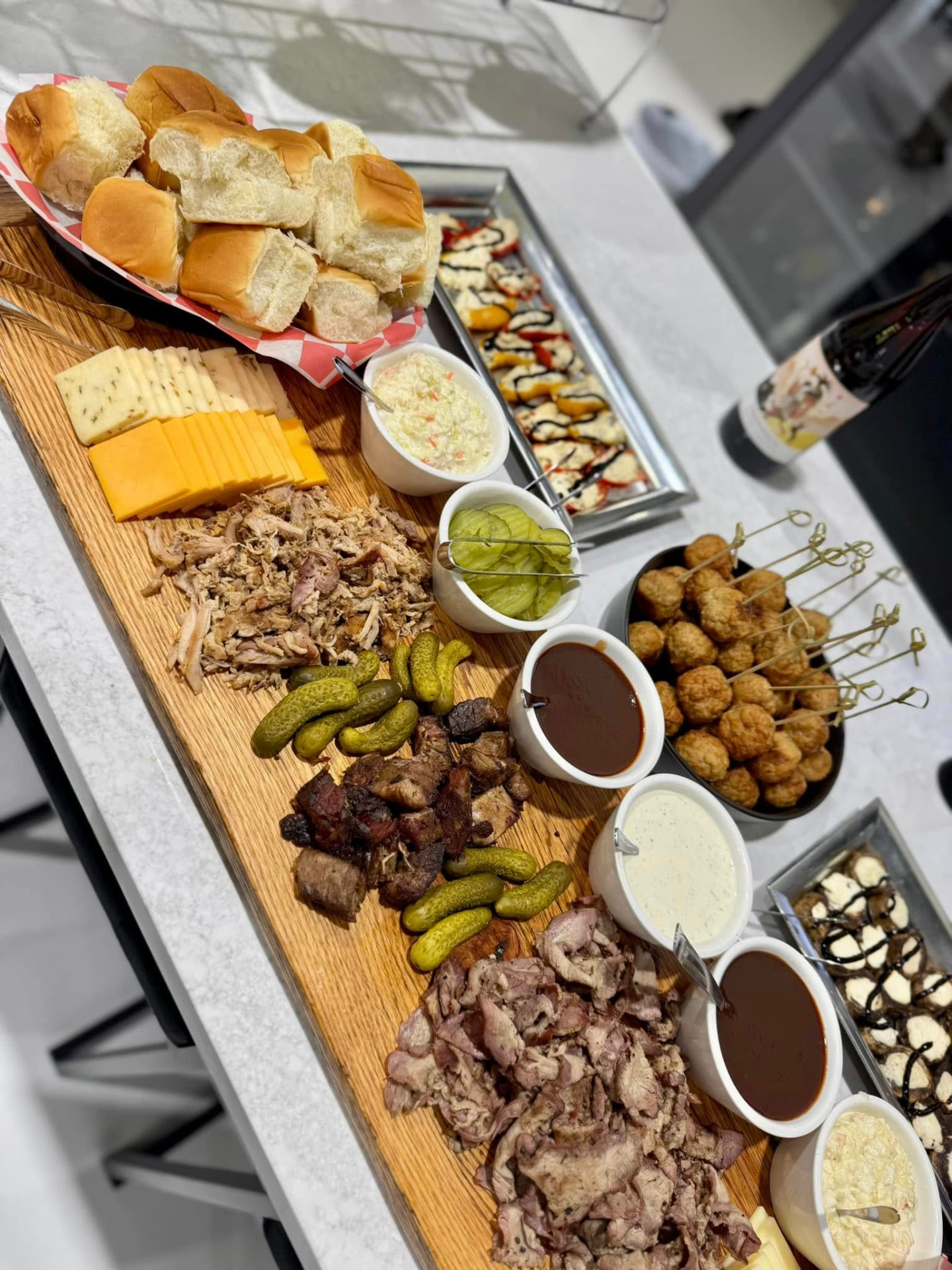 BBQ catering spread with smoked meats, cheeses, pickles, sauces and rolls